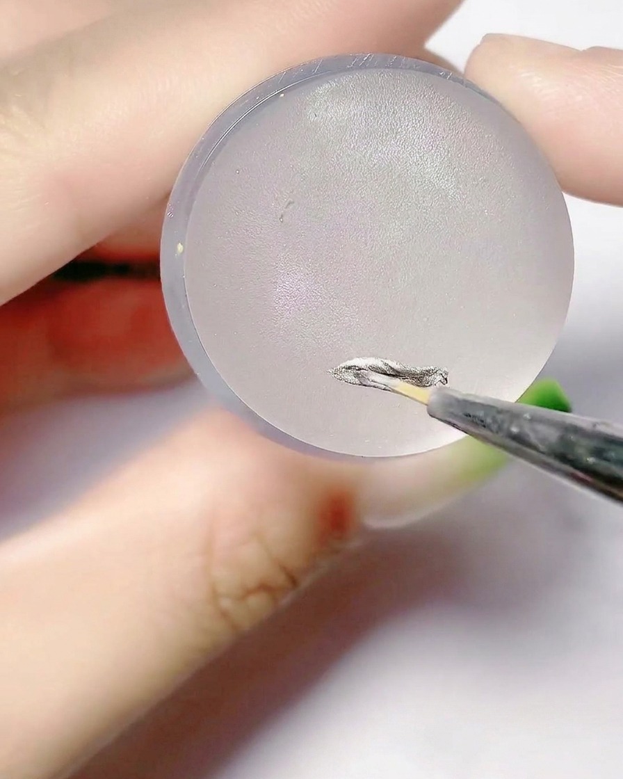 Un pennello fine applica il gel argento sulla superficie piatta di un cuscinetto per timbri in silicone.