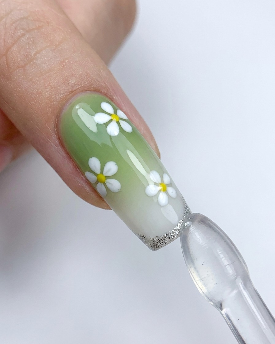 Ununghia decorata con fiori bianchi viene premuta contro un timbro in silicone per applicare una french tip argentata.
