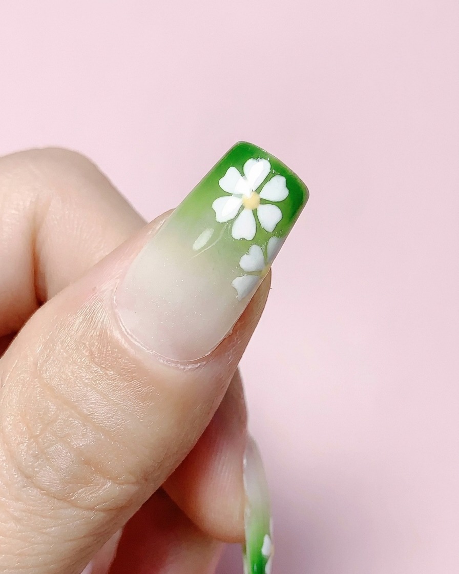 Ununghia quadrata finita con sfumatura verde e fiori bianchi rivestita con un top coat trasparente.