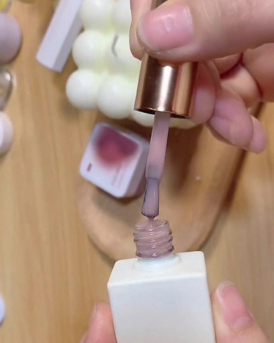 Un pennello estrae la base coat rosa traslucida da un flacone di smalto bianco.