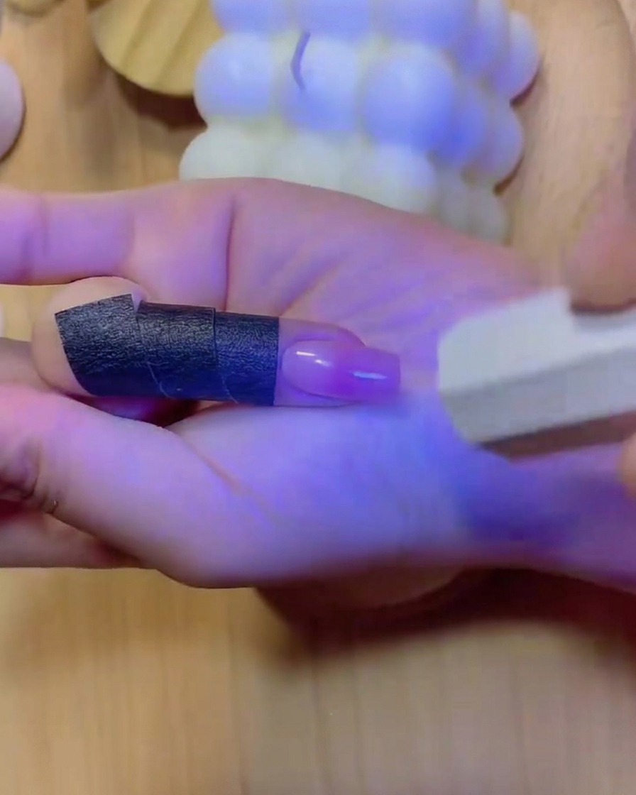 Una mano posizionata allinterno di una lampada per unghie UV/LED con luce blu che illumina le dita e lunghia sfumata curata.