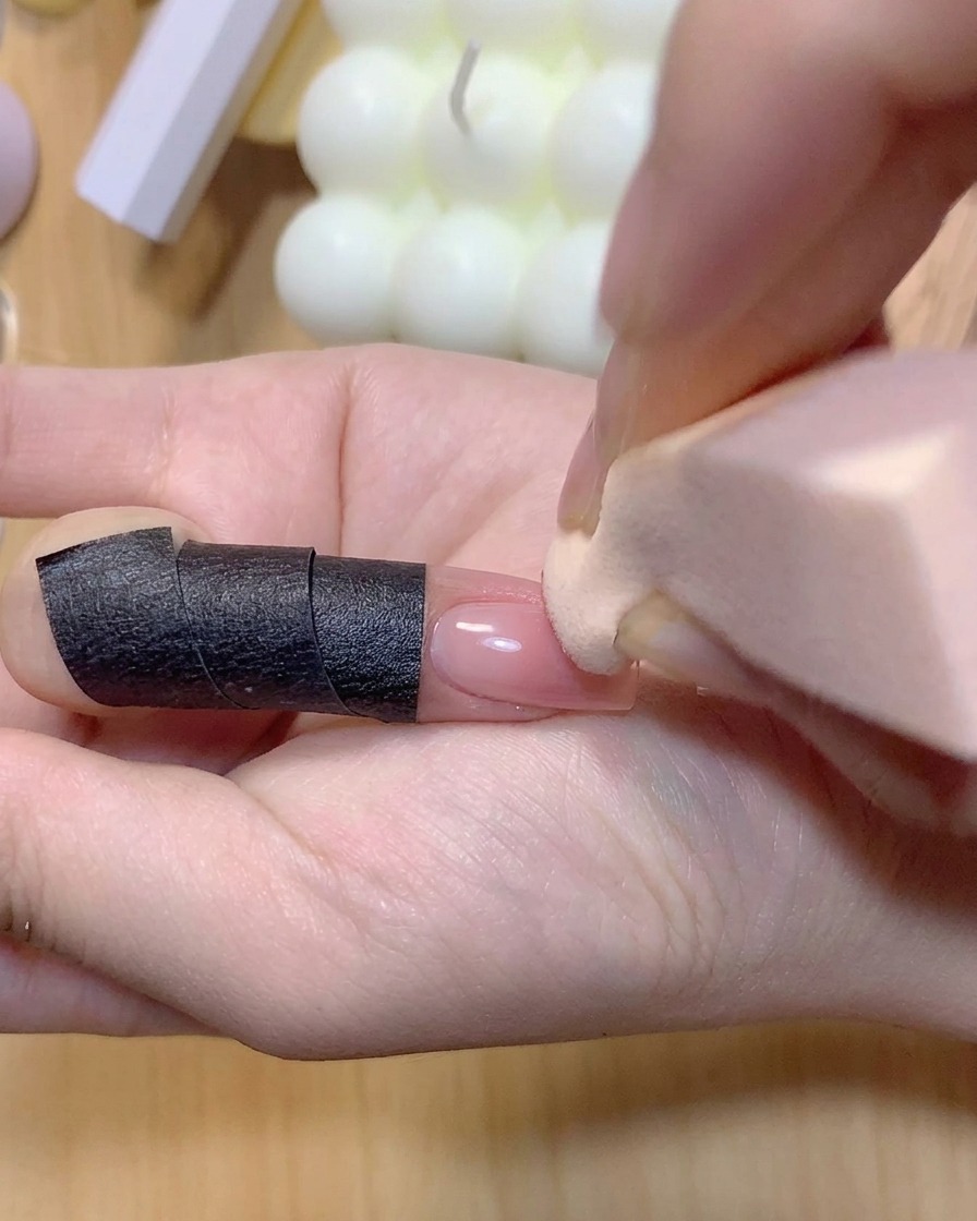 Una spugnetta per trucco tampona il colore rosa su ununghia per intensificare il gradiente ombre.