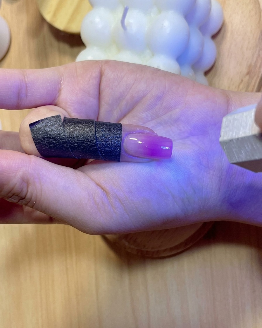 Ununghia che brilla sotto una luce viola UV/LED mentre polimerizza il gel di rinforzo applicato.