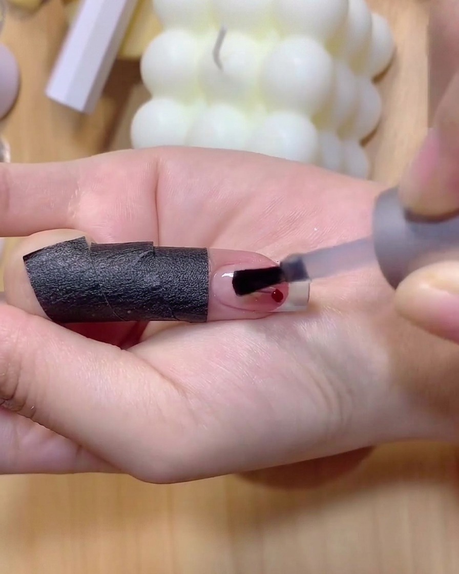 Un pennello fine per unghie applica smalto gel marrone chiaro per disegnare sottili steli di ciliegie su ununghia.