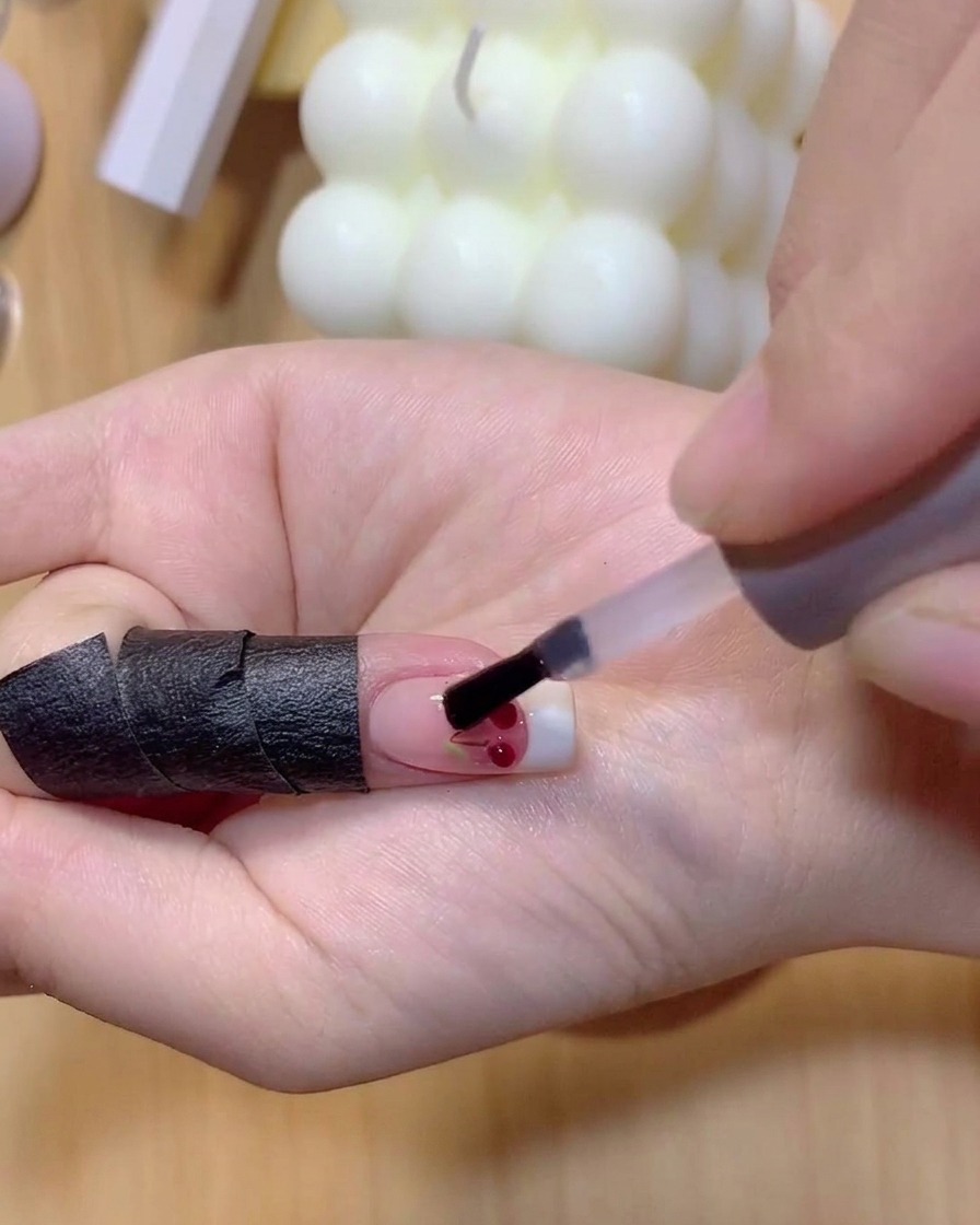 Un pennello applica smalto gel rosso traslucido sopra le sfere di ciliegia 3D trasparenti.
