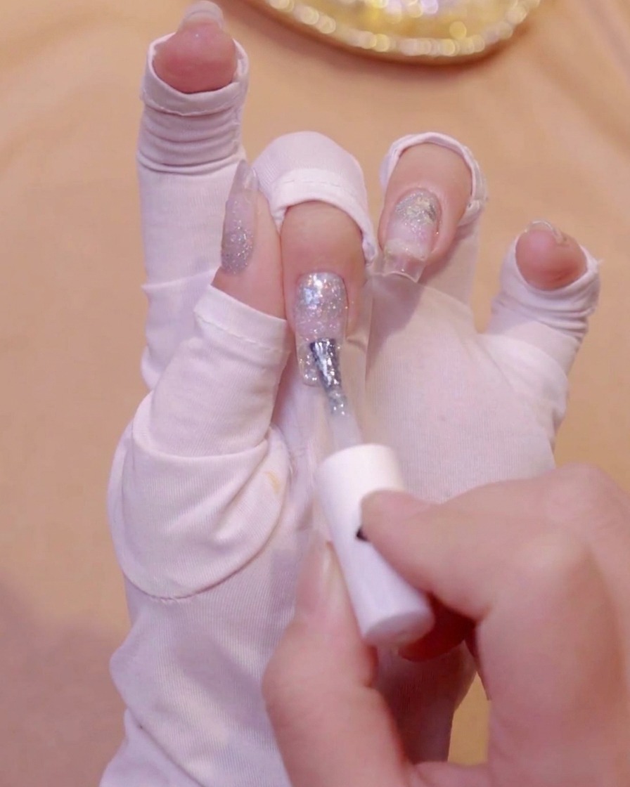 Una mano con guanti bianchi che usa un pennello per applicare lo smalto in gel bianco latte sulla punta di ununghia.