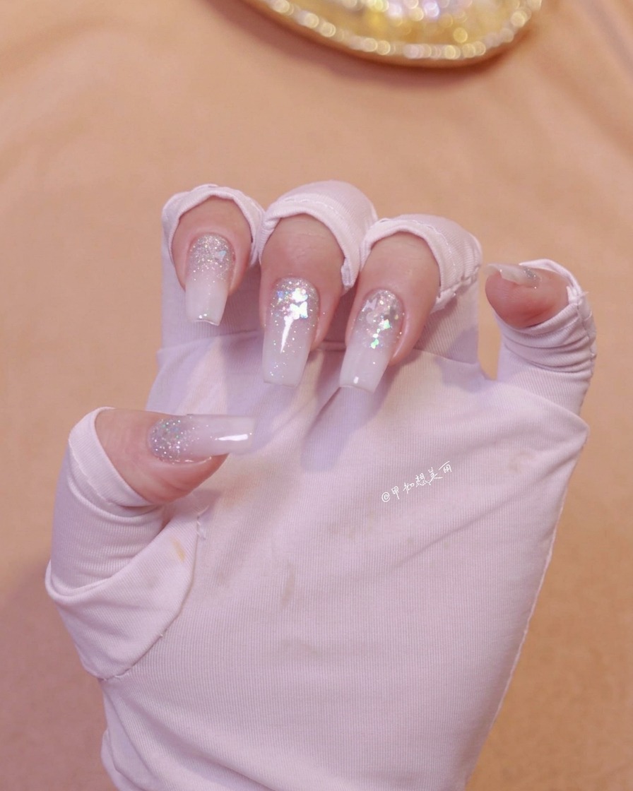 Una mano posizionata sotto una lampada per unghie per polimerizzare lo strato di nail art bianco latte appena applicato.