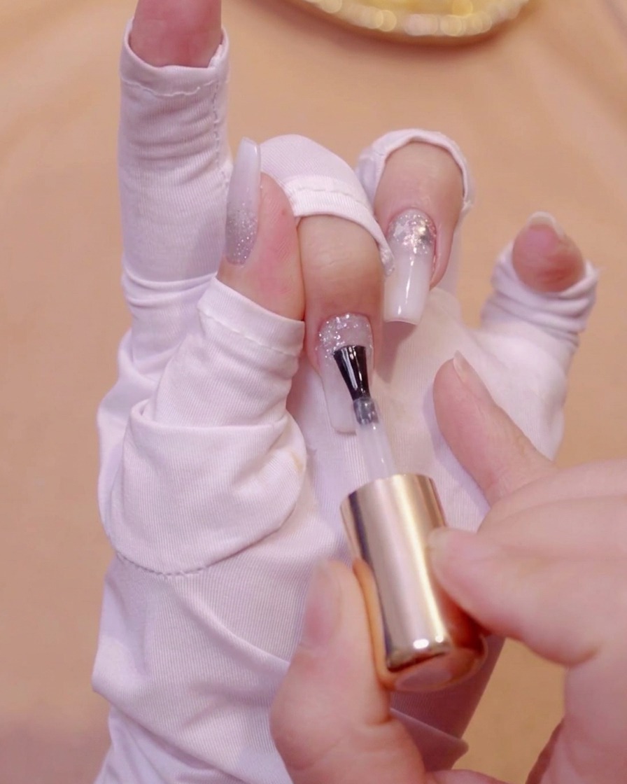 Un pennello che applica gel livellante trasparente su una superficie di unghia glitterata strutturata.