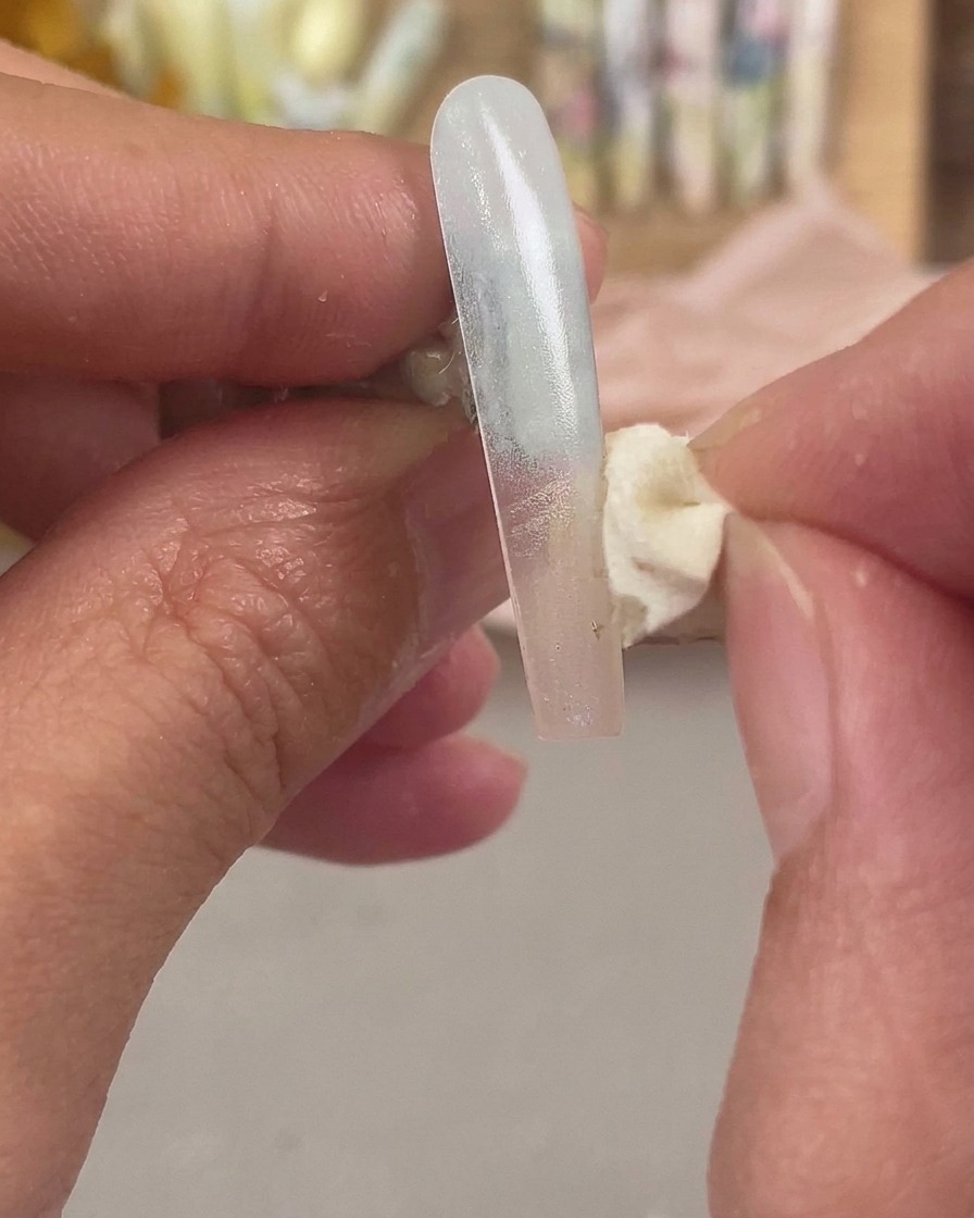 Una spugnetta cosmetica che tampona un colore secondario sulla punta dellestensione dellunghia per sfumare leffetto ombré.