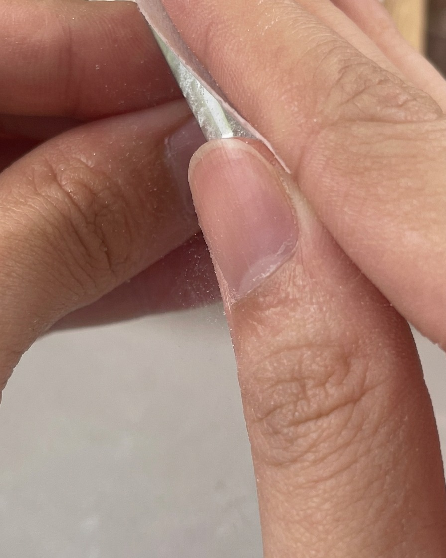 Dita che usano una salvietta bianca priva di pelucchi per pulire i residui appiccicosi da ununghia in gel trasparente appena polimerizzata.