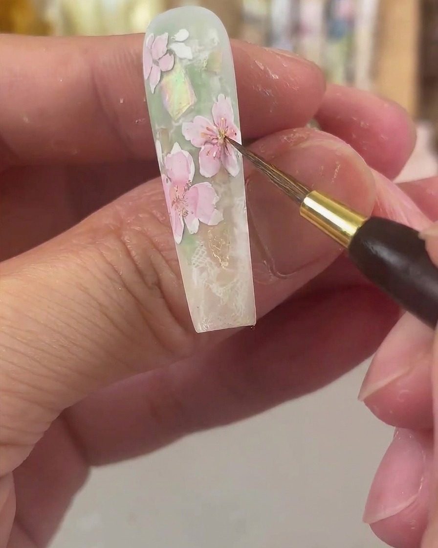 Un pennello da dettaglio fine che tampona acquerello giallo brillante al centro dei petali floreali tinti di rosa.