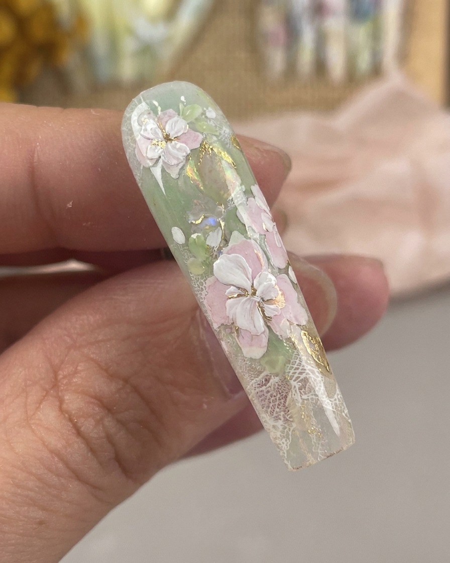 Una vista in primo piano di un pennello per nail art ultra-fine che disegna delicati dettagli di stami bianchi e punti centrali su un design floreale.