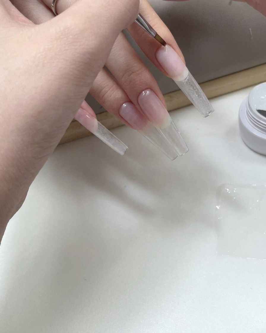 Un pennello fine per nail art che applica gel trasparente sulla parte inferiore di una lunga tip trasparente.