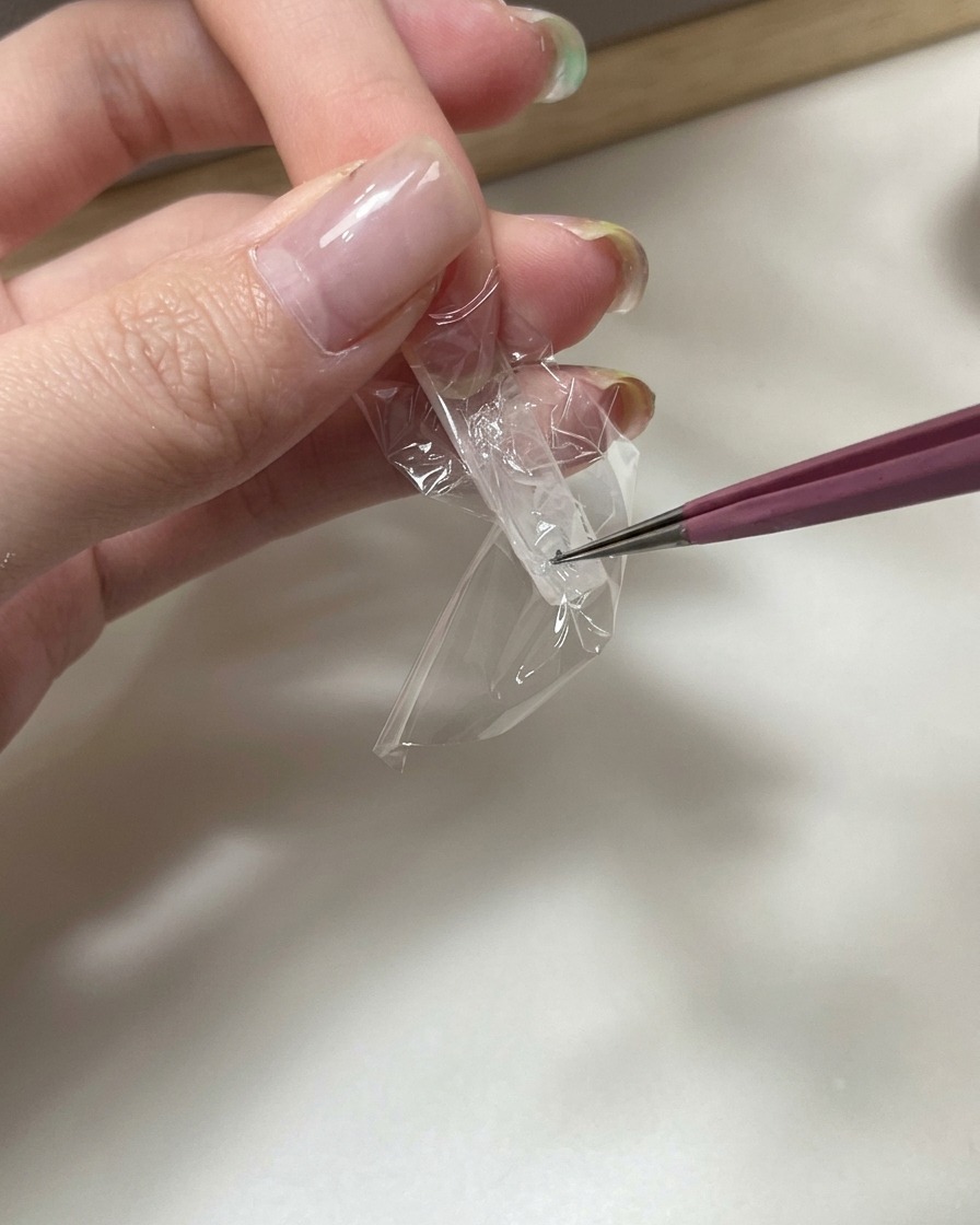 Primo piano di pinzette che premono un pezzo di pellicola trasparente nella parte inferiore di unestensione trasparente per creare una texture stropicciata.