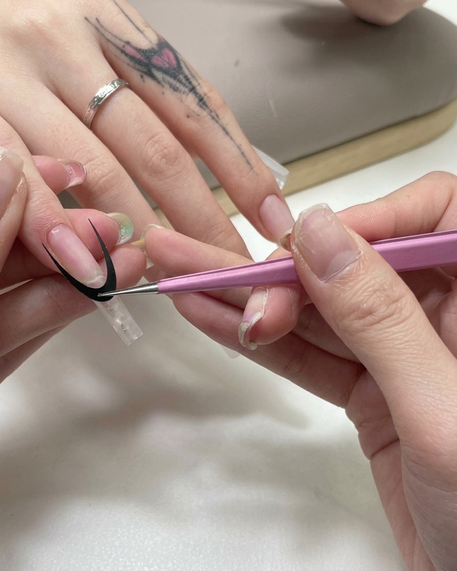 Pinzette rosa che applicano un adesivo guida curvo nero per french su unestensione trasparente dellunghia.