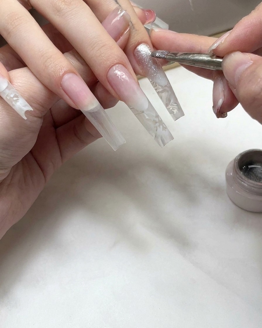 Un pennello per unghie che applica uno strato di gel cat-eye scintillante sulla sezione della punta di ununghia ricostruita.
