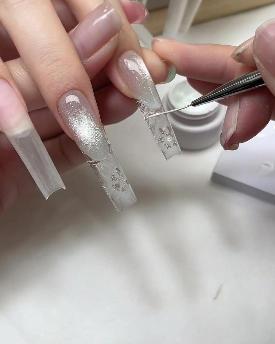 Un pennello fine per nail art che disegna dettagli di fiocchi di neve bianchi su unestensione trasparente testurizzata.