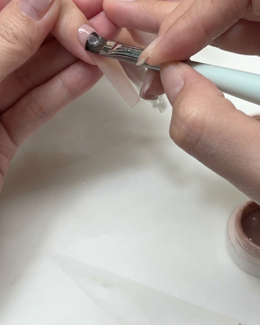 Un pennello piatto che applica gel nude per modellare una linea del sorriso french su ununghia.