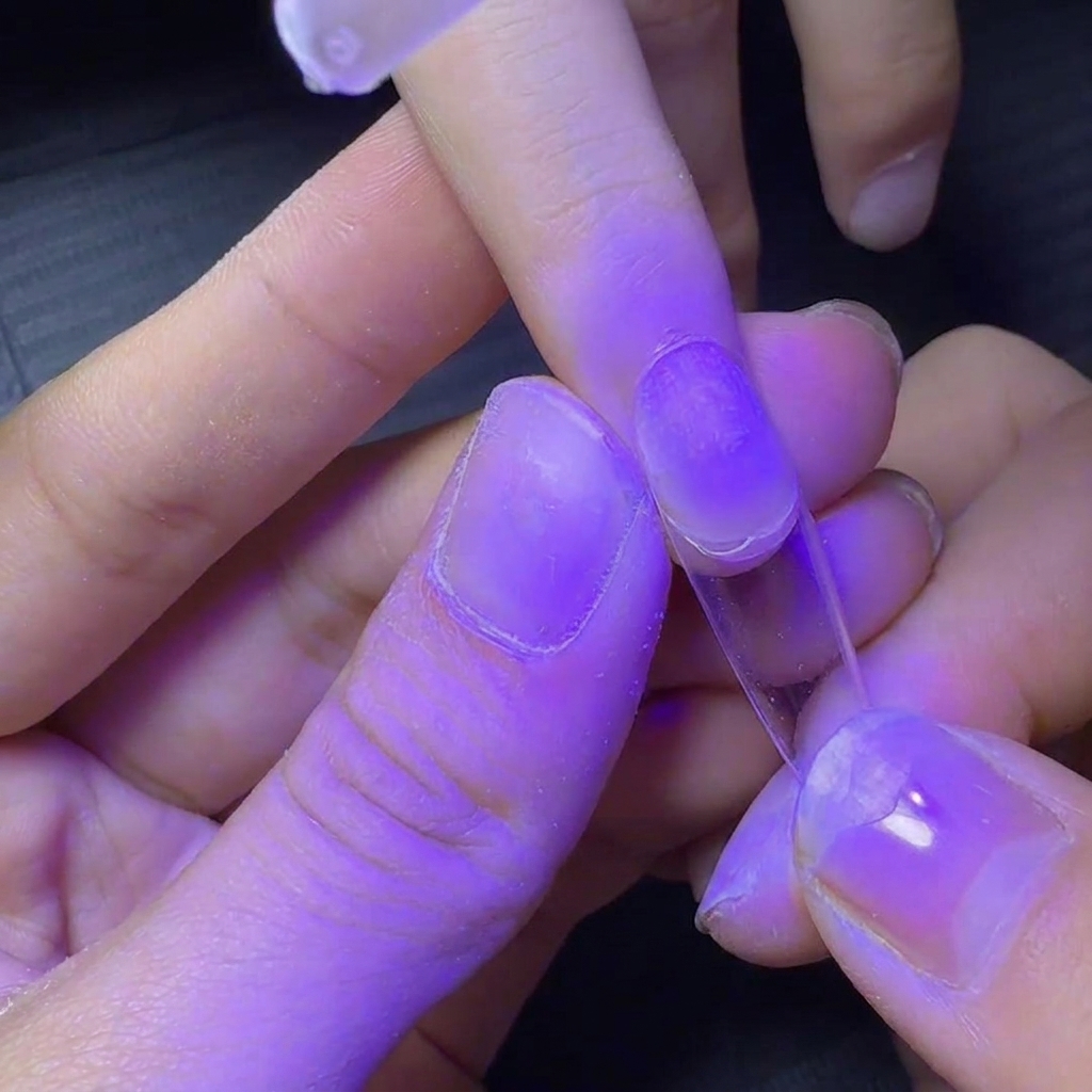Ununghia con tip trasparente tenuta sotto una lampada UV viola per una polimerizzazione flash rapida.