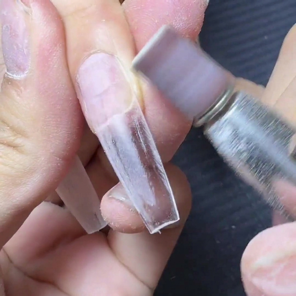 Una fresa elettrica dotata di un cilindretto abrasivo viola che leviga larea di connessione in cui la tip si unisce allunghia.