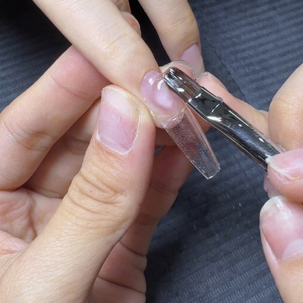 Un pennello da unghie che fa fluttuare e trascina il gel costruttore trasparente lungo la lunghezza di una tip di allungamento.