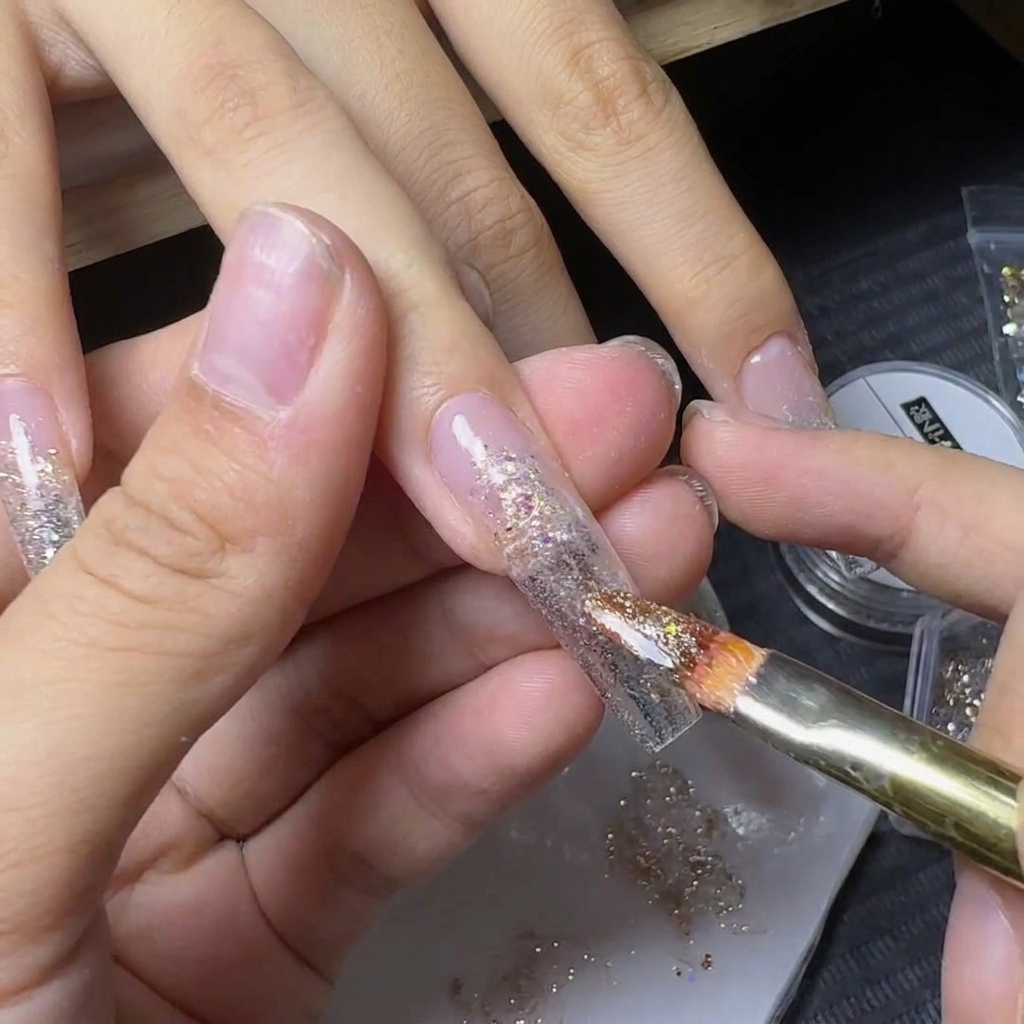 Un pennello che applica scaglie di glitter giallo-oro scintillanti sopra il centro di ununghia decorata.