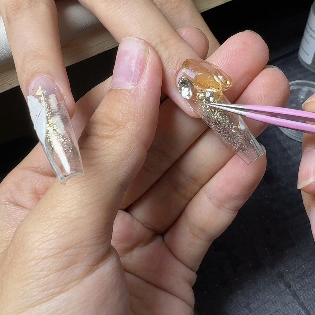 Pinzette di precisione che posizionano piccoli strass di cristallo attorno a una grande gemma centrale su ununghia glitterata.