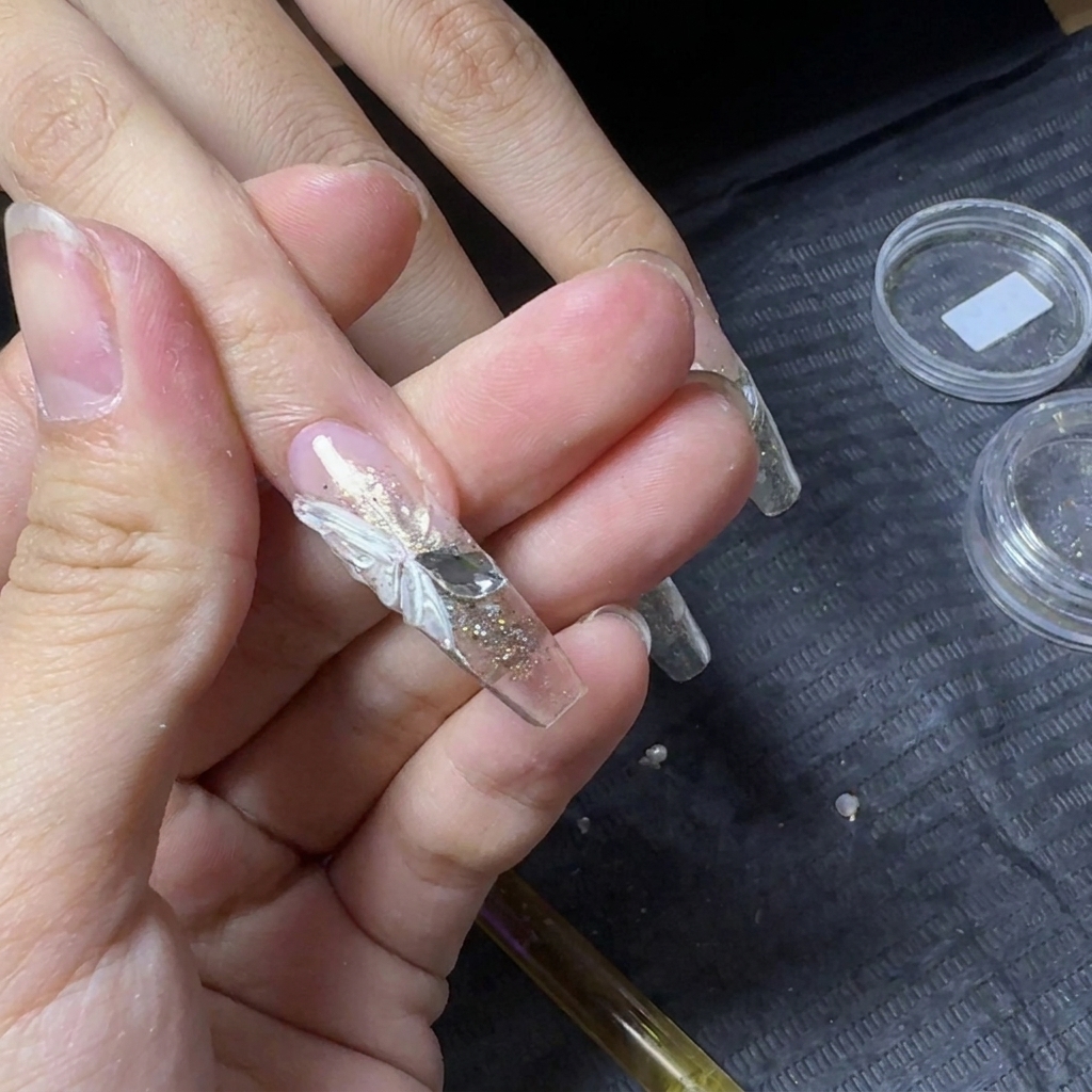 Un primo piano di unestensione trasparente con unala di farfalla 3D bianca e due strass piatti posizionati accanto per formare il corpo della farfallacite: 1.