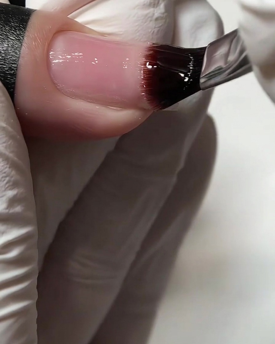 Un primo piano di un pennello per gel che applica una base trasparente su ununghia naturale.