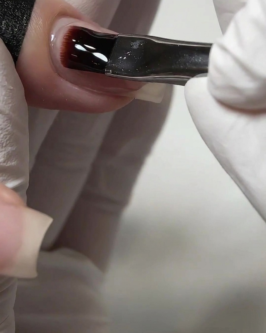 Un pennello che applica uno strato spesso di gel costruttore autolivellante trasparente su ununghia.