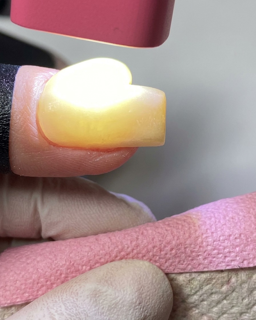 Una lampada UV portatile rosa che polimerizza lo smalto gel giallo su ununghia.