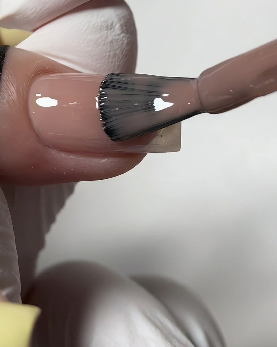 Un pennello della boccetta che applica uno smalto gel nude semitrasparente e lucido su ununghia preparata.