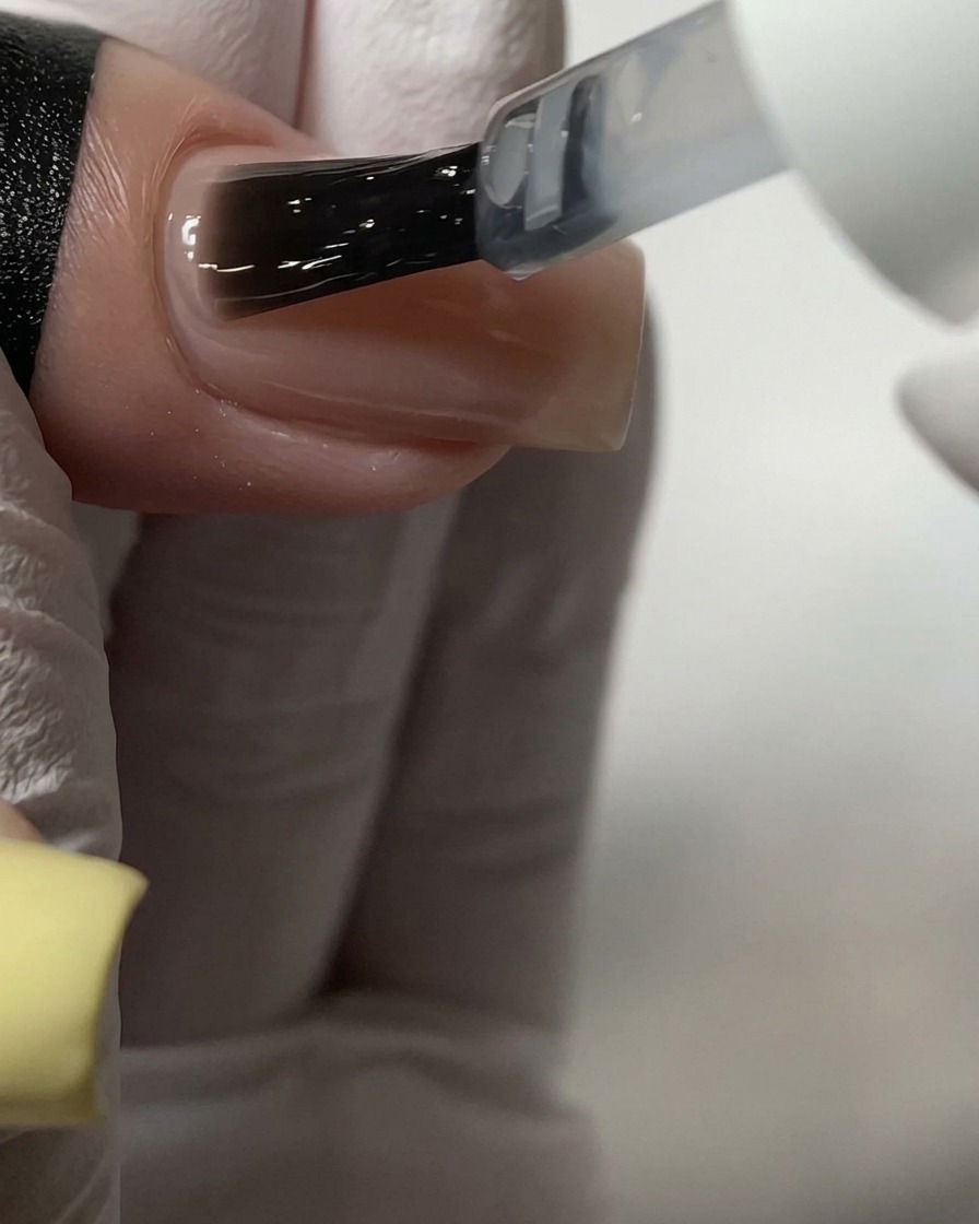 Un pennello che applica un top coat trasparente su ununghia in acrilico color nude.
