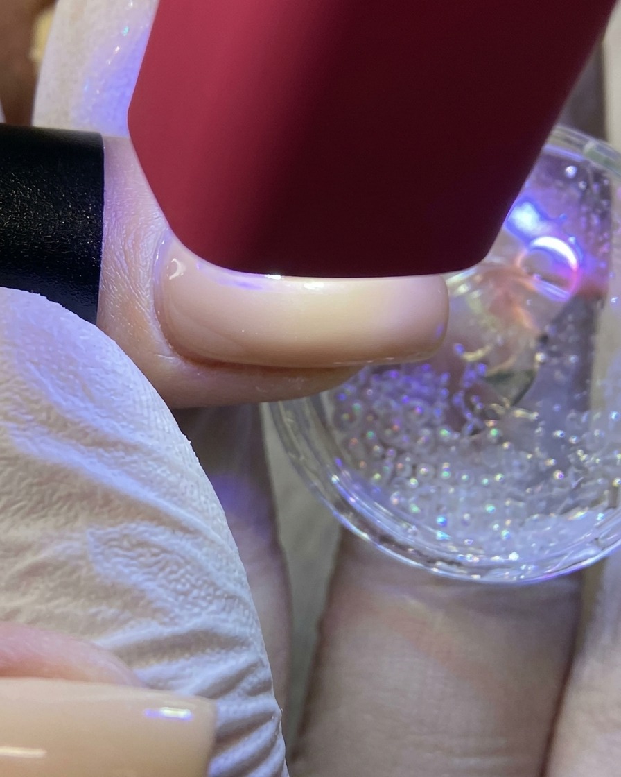 Una lampada UV/LED portatile rossa che illumina ununghia per polimerizzare un design a stella bianco ricoperto di glitter.