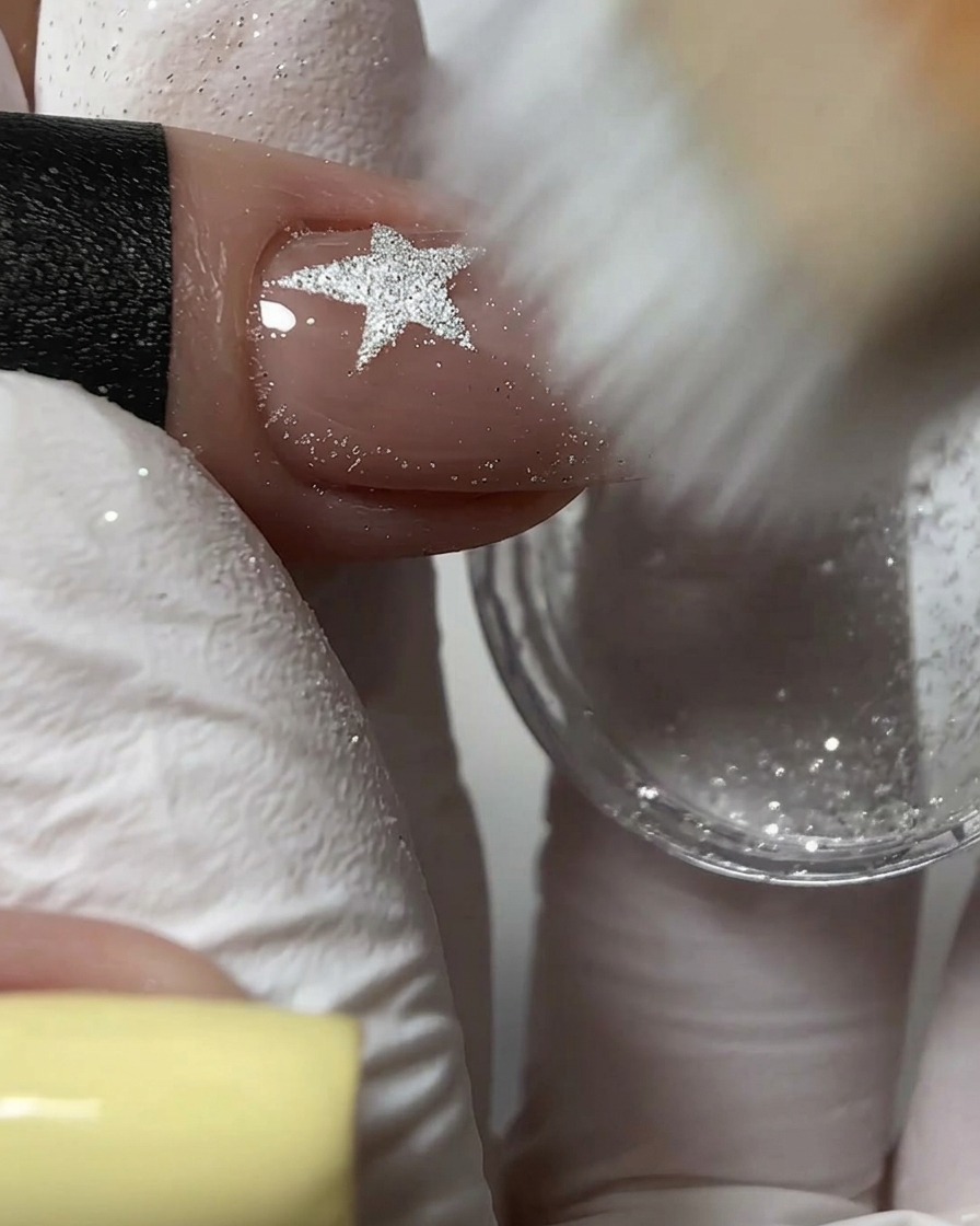 Una spazzolina a setole rigide che spazza via la polvere glitter argento in eccesso da un design per unghie in rilievo.