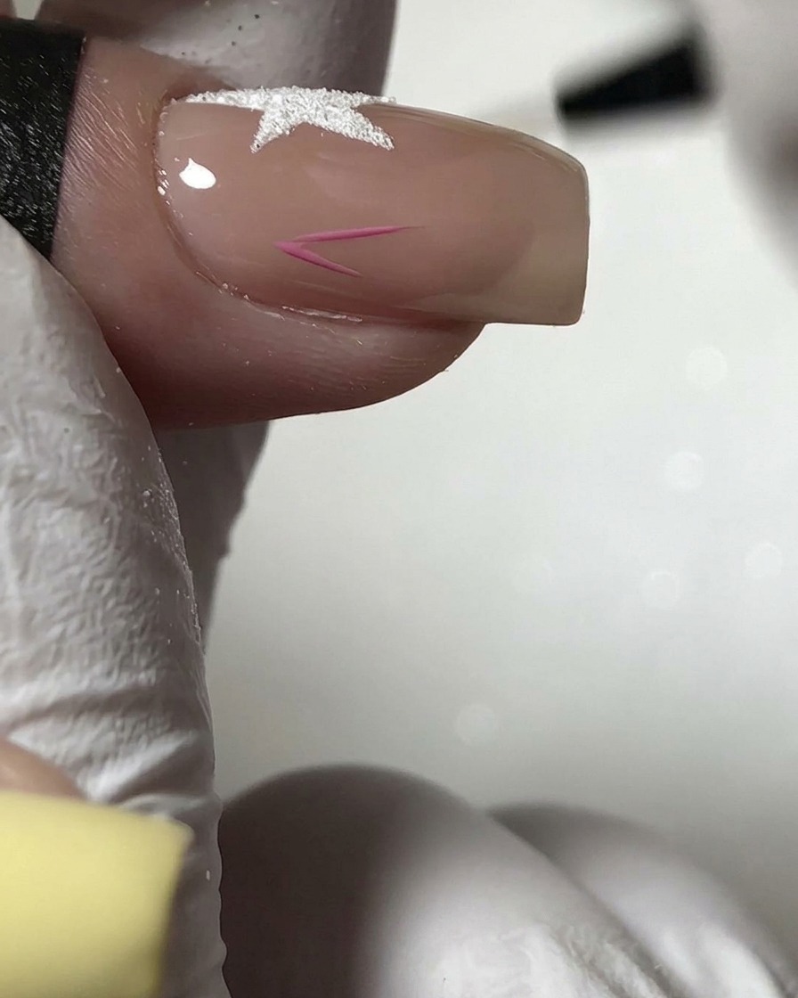 Un pennello fine che dipinge il contorno di una piccola stella rosa sulla sezione inferiore di ununghia nude.