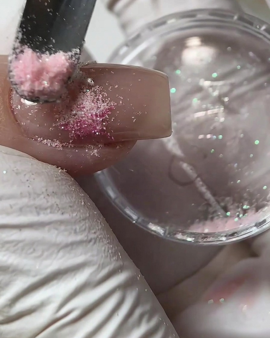 Un piccolo strumento che sparge polvere di zucchero rosa su un design in gel bagnato su ununghia.