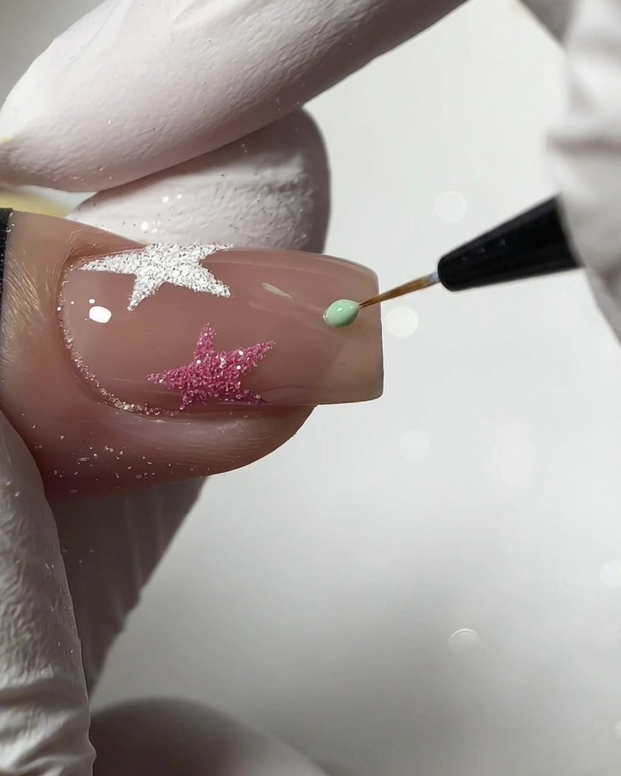 Un pennello liner fine che applica una piccola goccia di gel verde menta per creare una stella su ununghia nude.