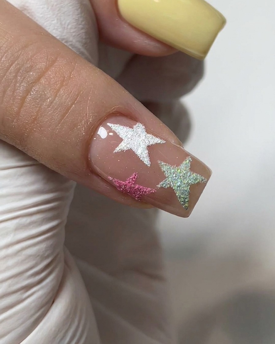 Un pennello che applica un top coat lucido trasparente su ununghia decorata con polvere cromo e stelle in rilievo.