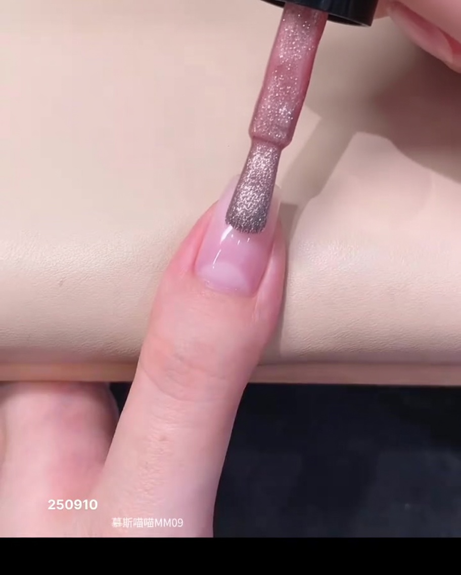 Un pennellino che applica una goccia di smalto semipermanente magnetico rosa trasparente vicino alla zona delle cuticole di ununghia naturale.