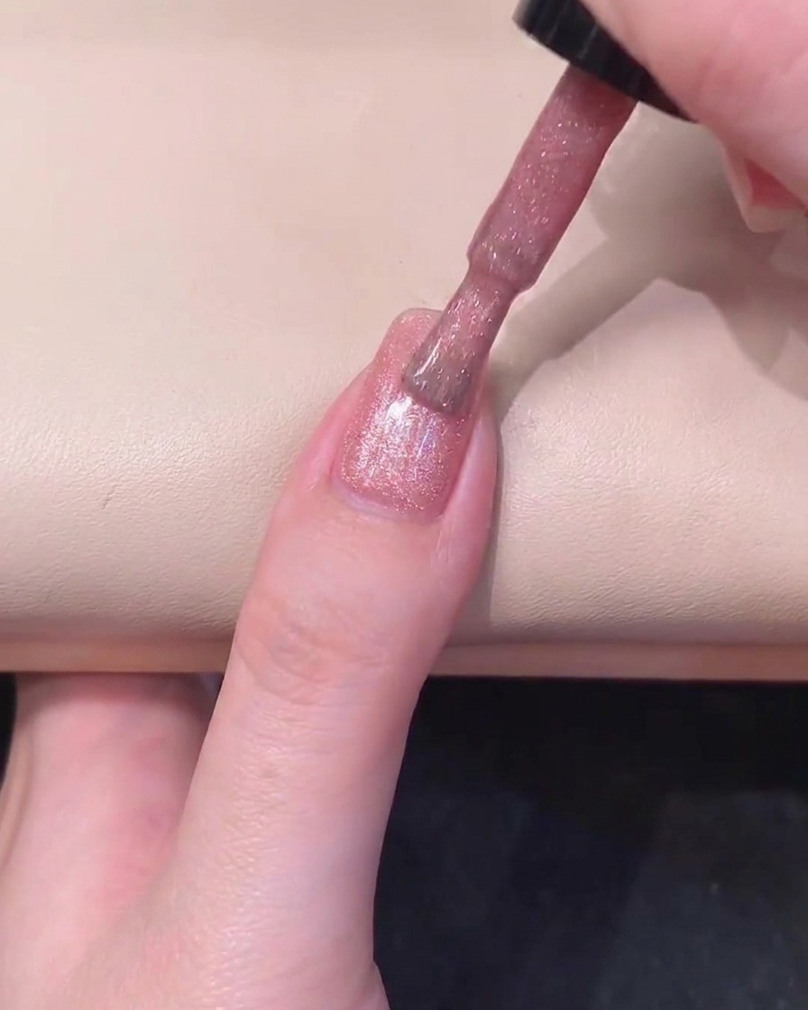 Un magnete cilindrico nero tenuto parallelamente al lato destro di ununghia rivestita di gel rosa per attivare il riflesso.