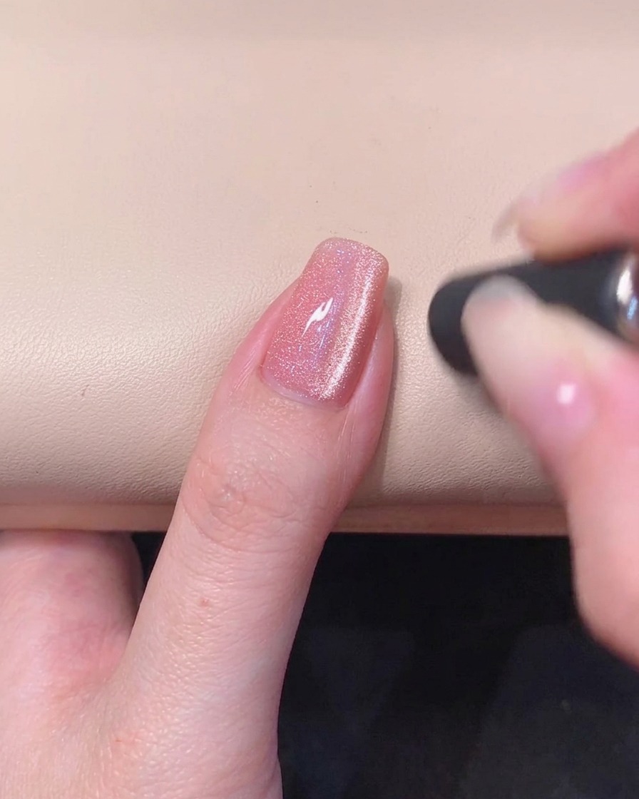 Un primo piano di ununghia in gel rosa con una striscia luminosa magnetica cat-eye visibile nella superficie del gel fresco.