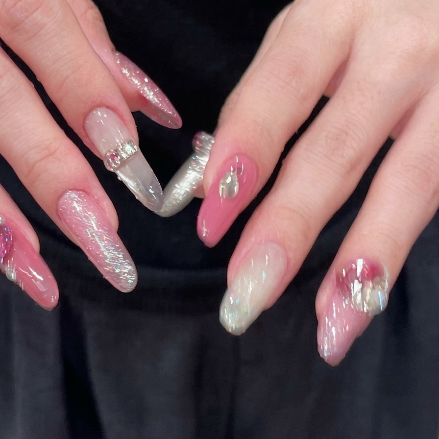 Un primo piano di mani con dita aperte, che rivelano unghie lunghe a mandorla rosa e argento completamente decorate con accenti di strass scintillanti.