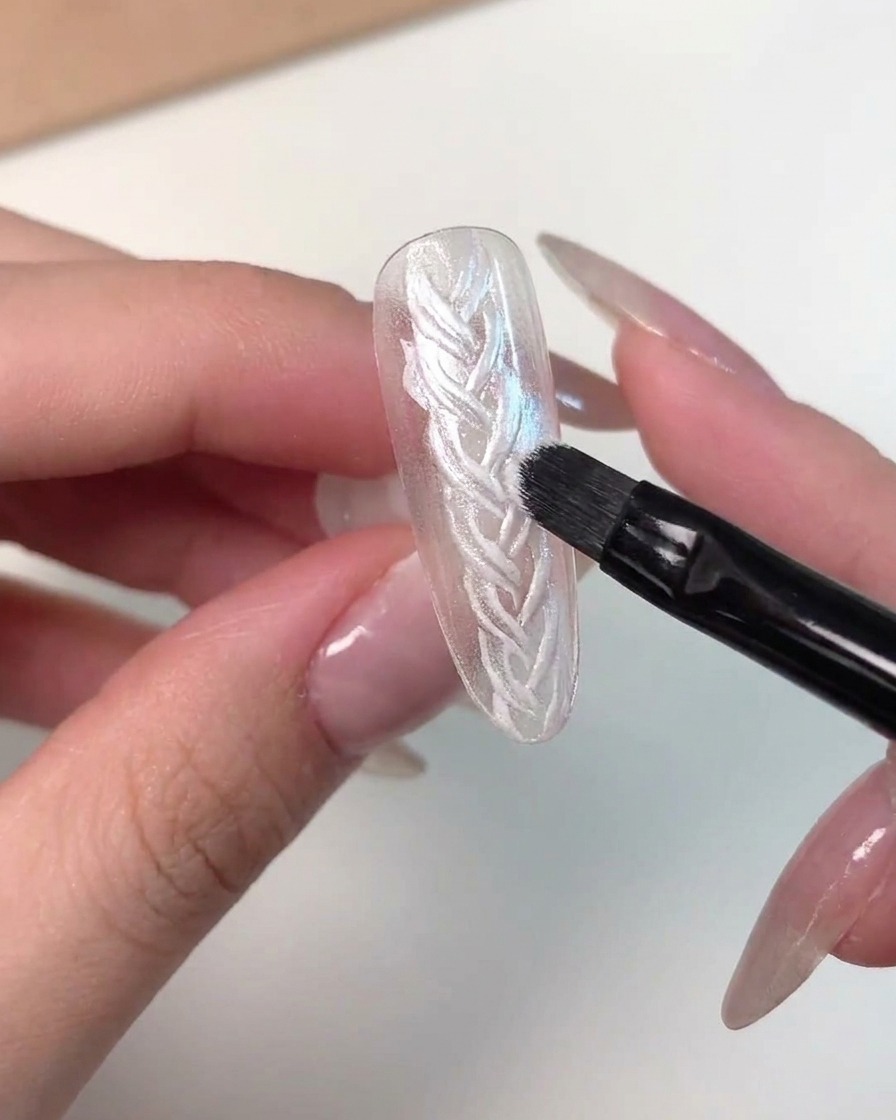 Un primo piano dettagliato che mostra un pennello mentre applica il gel cat eye rosa magnetico su una tip per unghie.
