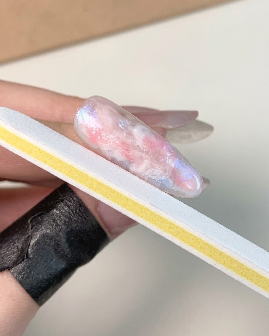 Una mano che tiene una lima per unghie bianca e gialla, opacizzando la superficie di ununghia in gel lucida e polimerizzata.