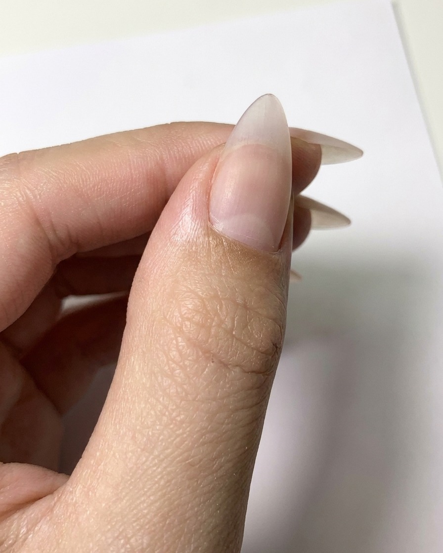 Un pennello a punta fine che applica contorni in gel bianco su una superficie di unghia nude opaca per formare le forme dei petali.