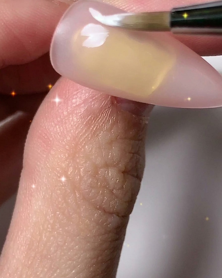 Un pennello per unghie che aggiunge petali bianchi per completare i contorni di più fiori sulla lamina ungueale.