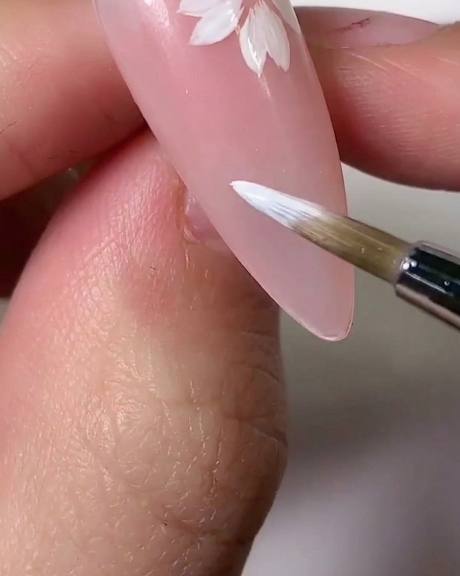 Un pennello che applica una tinta in gel rosa chiaro su sezioni dei petali bianchi per un effetto sfumato.