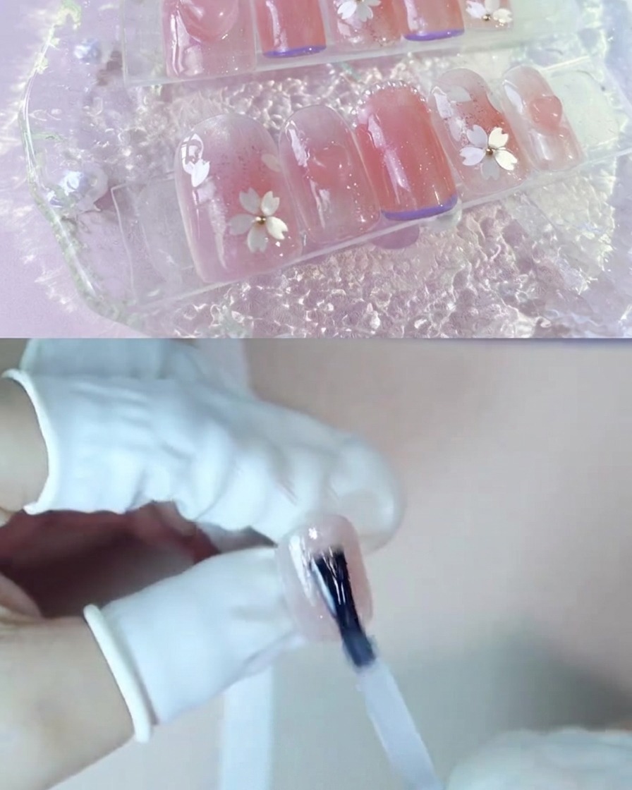 Una mano applica uno strato di gel trasparente di rinforzo su ununghia rosa blush.