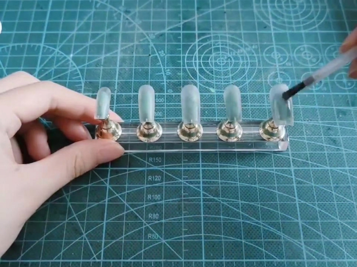 Un pennello applica uno strato di gel cat-eye traslucido su una tip per unghie.
